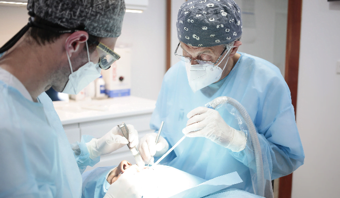 Dos dentistas con uniforme azul interviniendo a un paciente