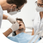 Dos dentistas con uniforme blanco interviniendo a un paciente